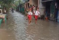 Dua orang siswa saat melintasi genangan air di Perumahan Mustika, Tigaraksa, Kabupaten Tangerang, Banten, Senin (6/5/2026)