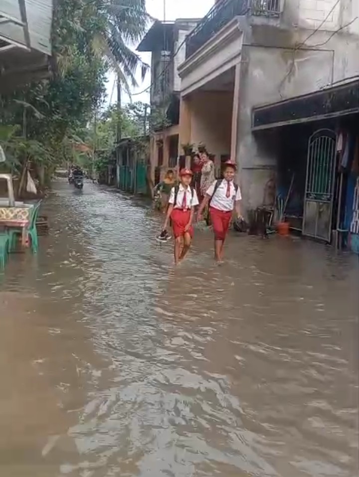 Dua orang siswa saat melintasi genangan air di Perumahan Mustika, Tigaraksa, Kabupaten Tangerang, Banten, Senin (6/5/2026)